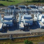 Eine weitläufige Industrieanlage mit mehreren großen Gebäuden, zahlreichen Rohrleitungen und Schornsteinen, umgeben von Grünflächen.