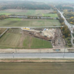 Eine Luftaufnahme einer Pipeline-Baustelle zeigt eine großflächige Baustelle mit umliegenden Feldern, Straßen und Bahngleisen.